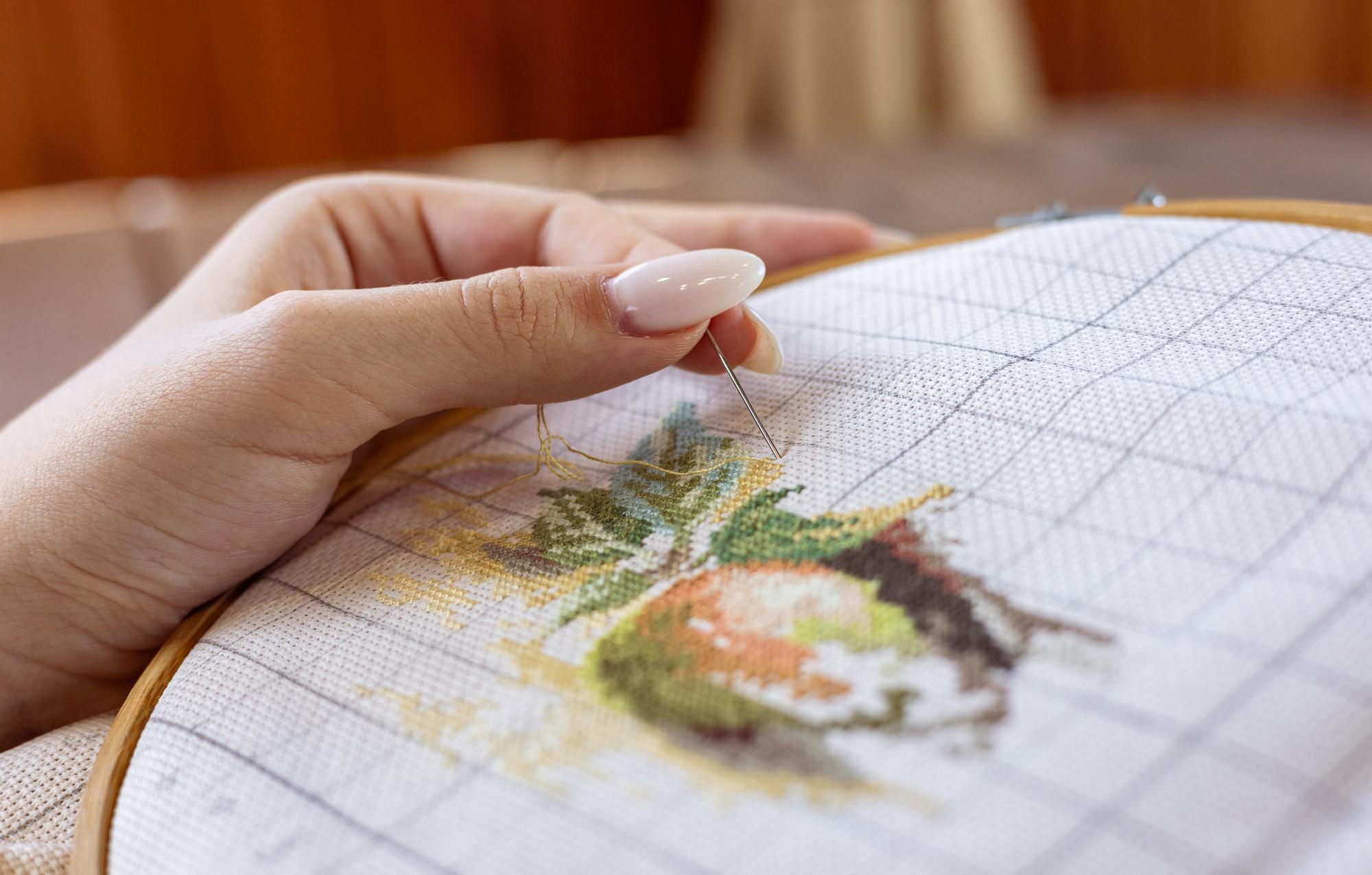 Mano che lavora ricamo botanico su tessuto naturale